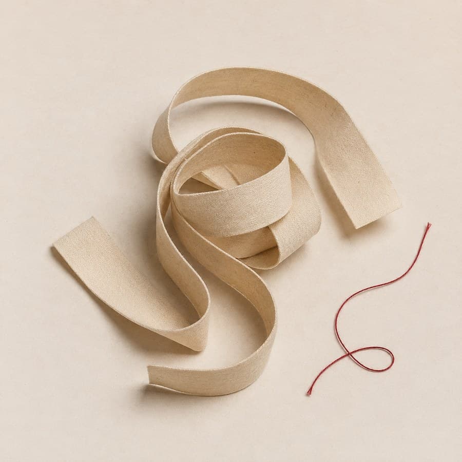 A coiled cloth tape measure and a single red thread on pale paper